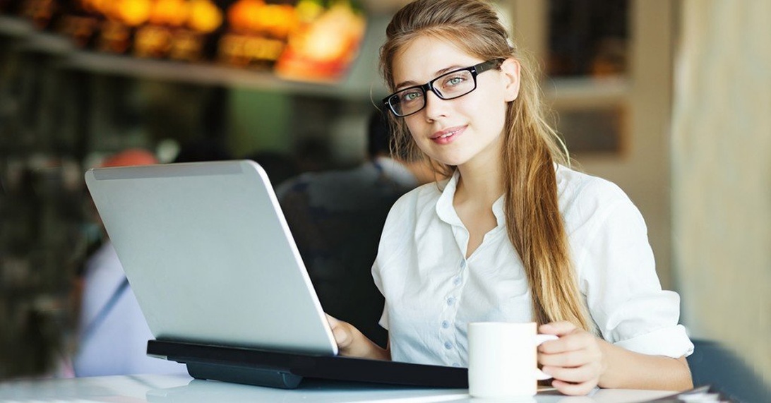 Kvinna med glasögon arbetar vid laptop på café.