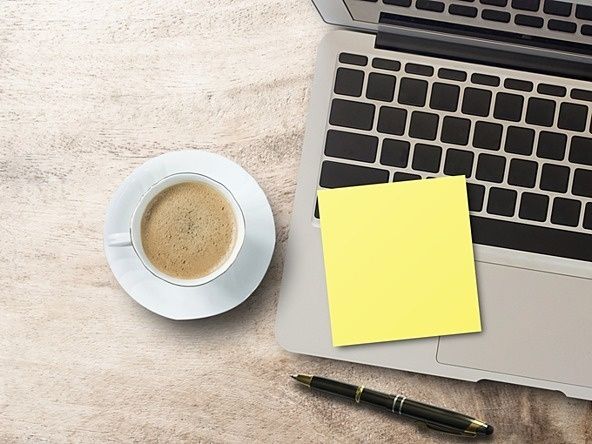 Laptop med gul anteckningslapp, kaffe och penna på ett skrivbord